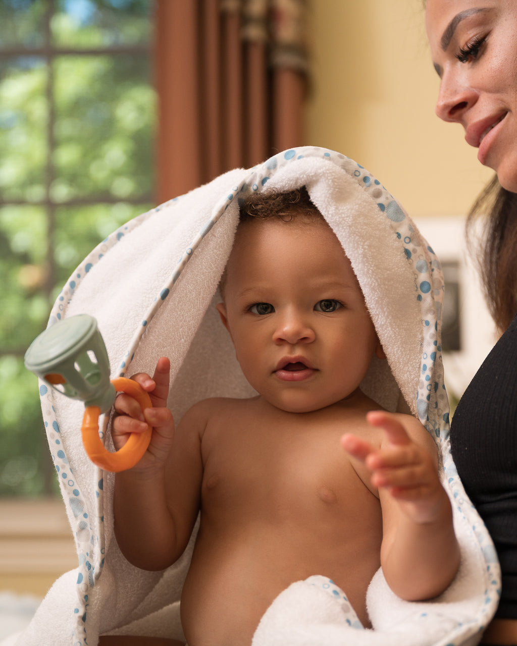 Baby seated on mother's lap in EleryB towel with blue trim and folded hood