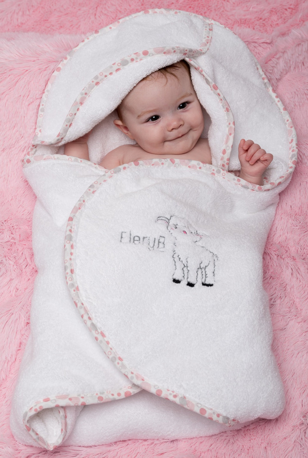 Infant swaddled in white EleryB hooded towel with pink geometric trim

