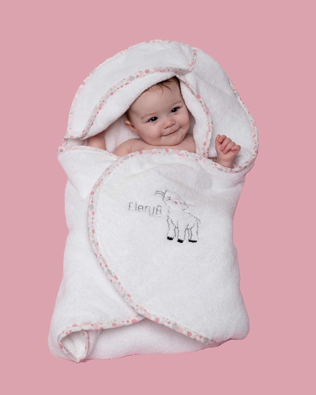 Infant swaddled in white EleryB hooded towel with pink geometric trim
