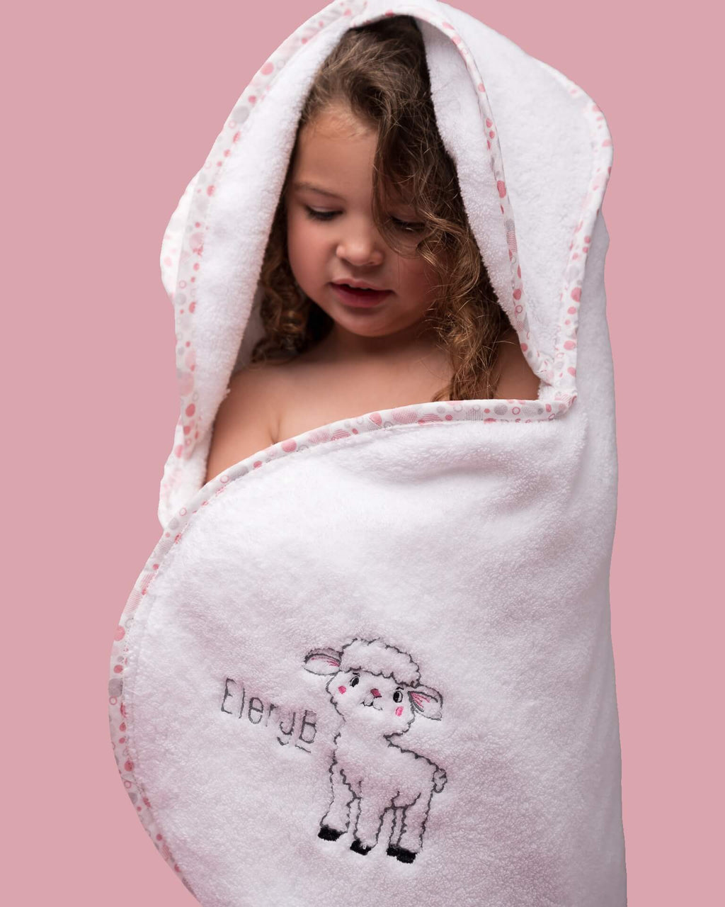 Toddler in EleryB hooded towel with pink geometric trim and lamb logo with folded back head flaps
