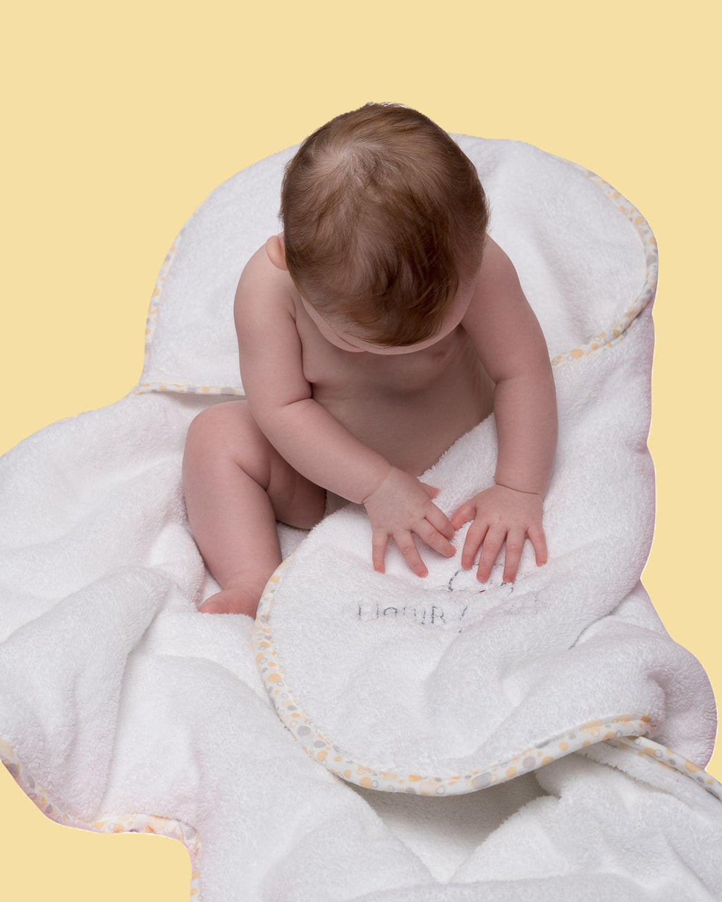 Luxury hooded baby towel with geometric yellow trim and embroidered lamb logo with seated baby
