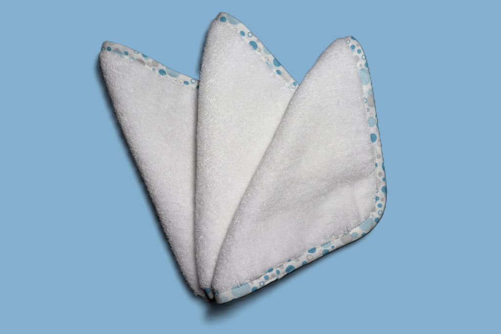 Three EleryB hypoallergenic washcloths with blue geometric trim, triangle fold
