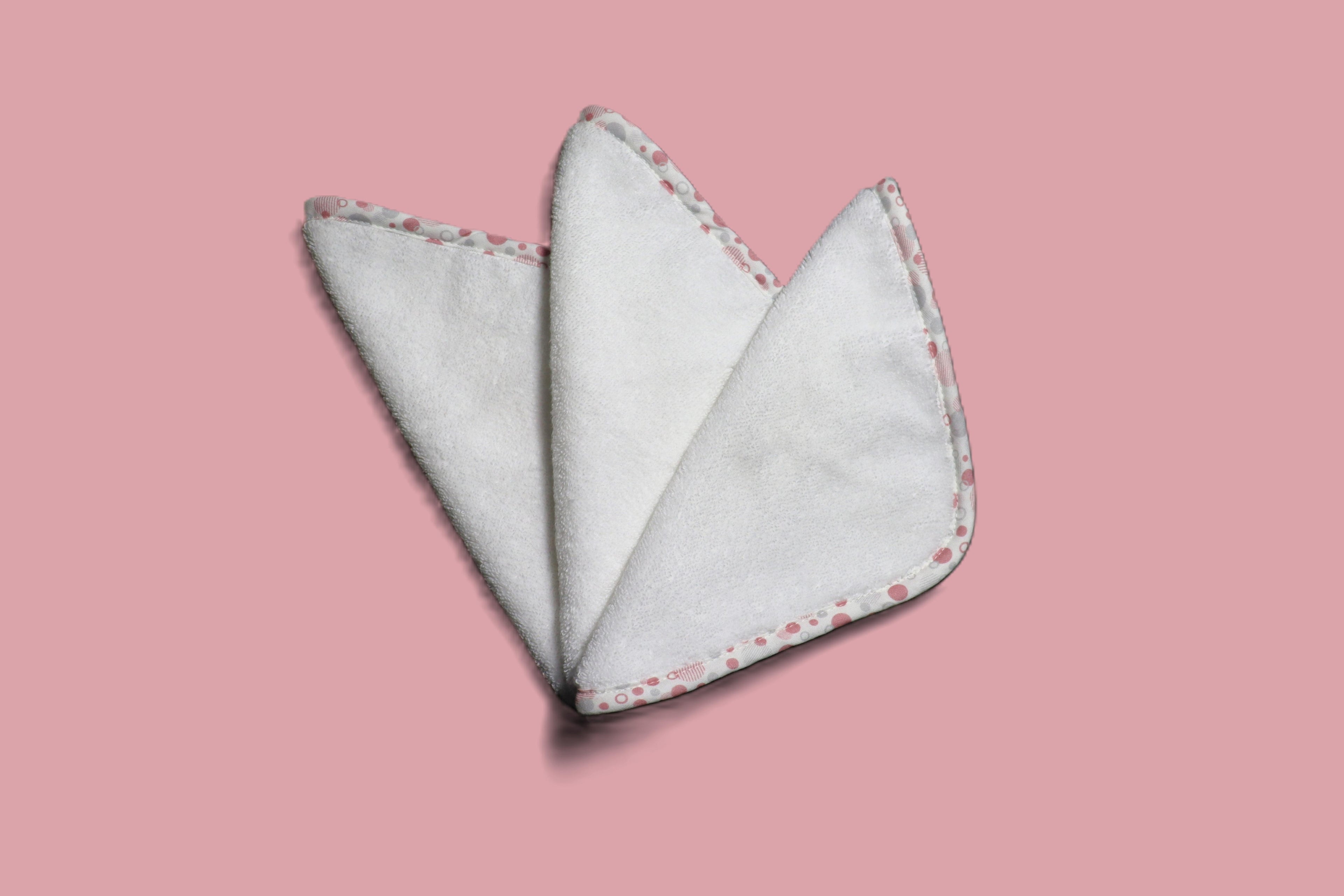 Three EleryB hypoallergenic washcloths with pink geometric trim, triangle fold
