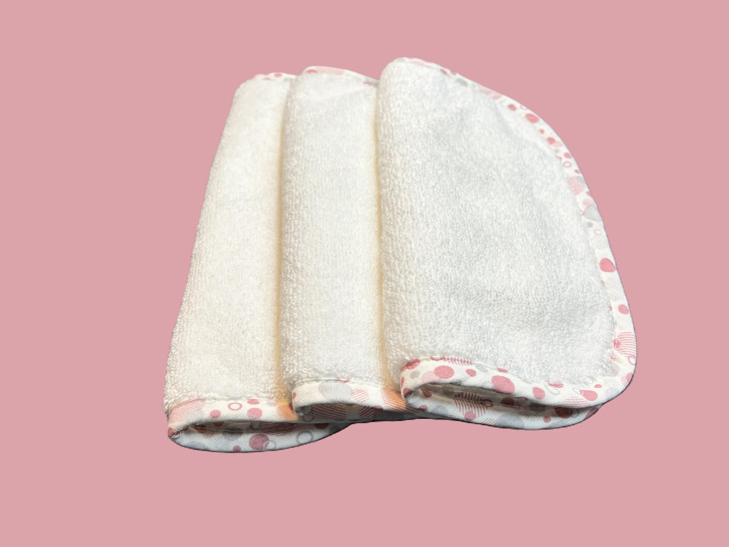 Three ultra-soft EleryB washcloths with pink geometric trim, folded and stacked
