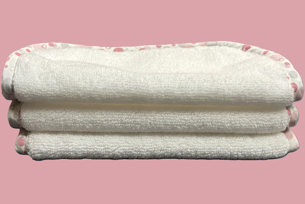 Three stacked white EleryB hypoallergenic washcloths with pink geometric trim, folded in half
