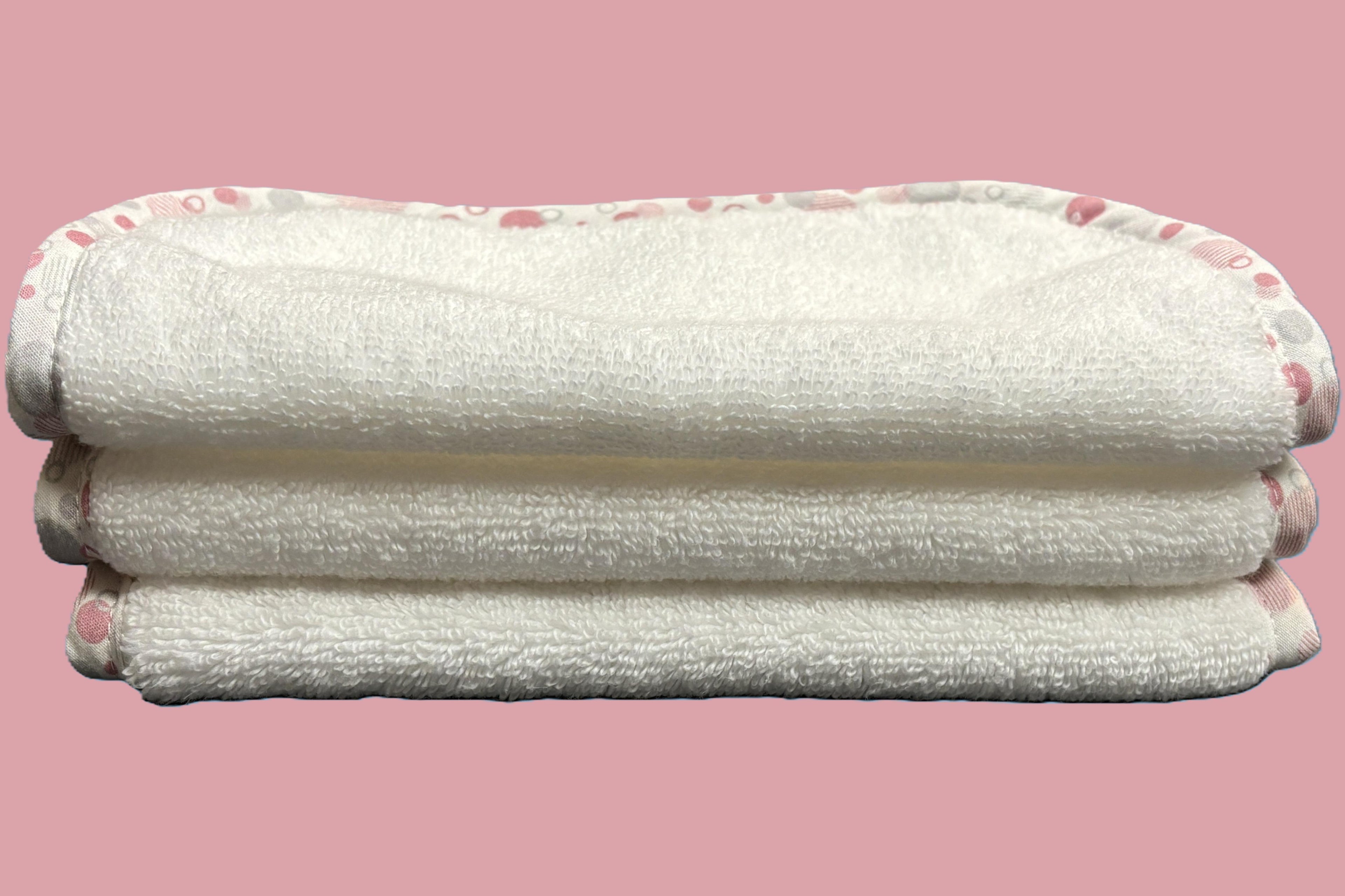 Three stacked white EleryB hypoallergenic washcloths with pink geometric trim, folded in half
