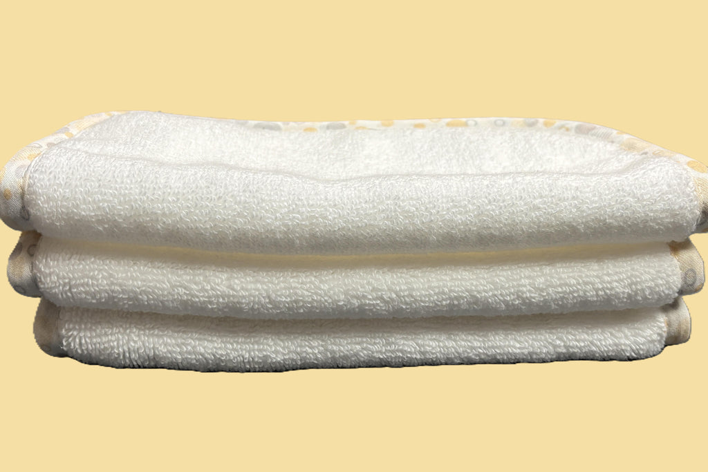 Three stacked white EleryB hypoallergenic washcloths with yellow geometric trim, folded in half

